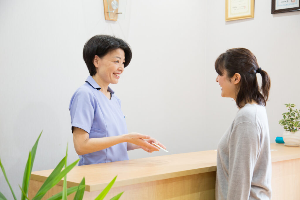 木目調の受付カウンターで、笑顔のスタッフが女性の来院者へ話しかけている様子|山下針灸房(姫路市)