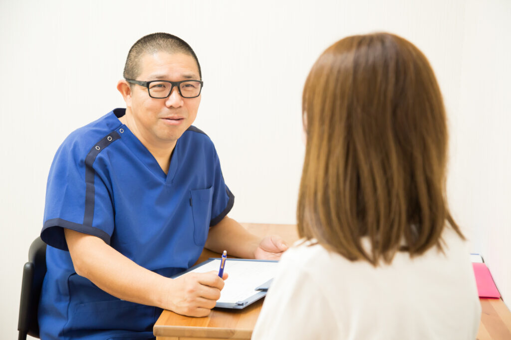 Step2:ネイビーの施術着を着た鍼灸師が机の向かいで、予診内容をもとに患者様へ問診・カウンセリングしメモを取る様子。これまでの治療、検査結果、体調の変化などを丁寧に伺う場面|山下針灸房(姫路市)