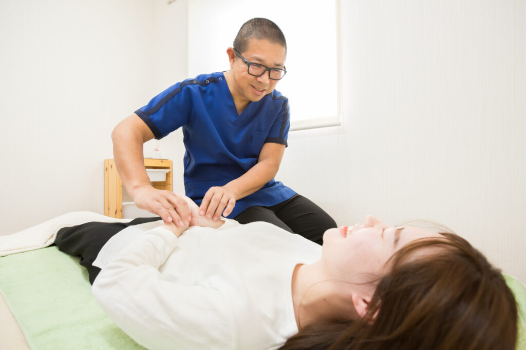 施術台に仰向けの患者様の腹部を、スクレルを着た鍼灸師が丁寧に確認している様子|山下針灸房(姫路市)