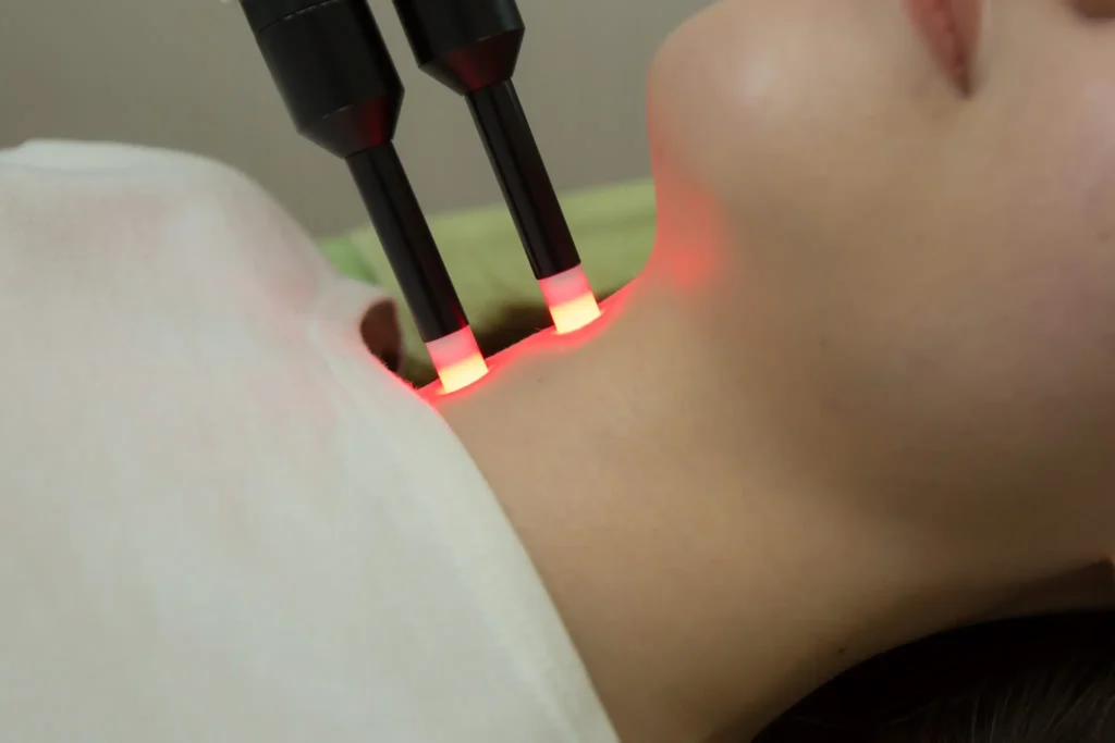 Step5:仰向けの患者様の喉元・首すじに、先端が赤く光る2本のプローブ(スーパーライザー)を当てて照射するクローズアップ。喉元の自律神経のポイントへ痛みの少ない最新レーザーを用い、短時間の照射で子宮環境と全身のめぐりを整える支援を行う内容のイメージ|山下針灸房(姫路市)